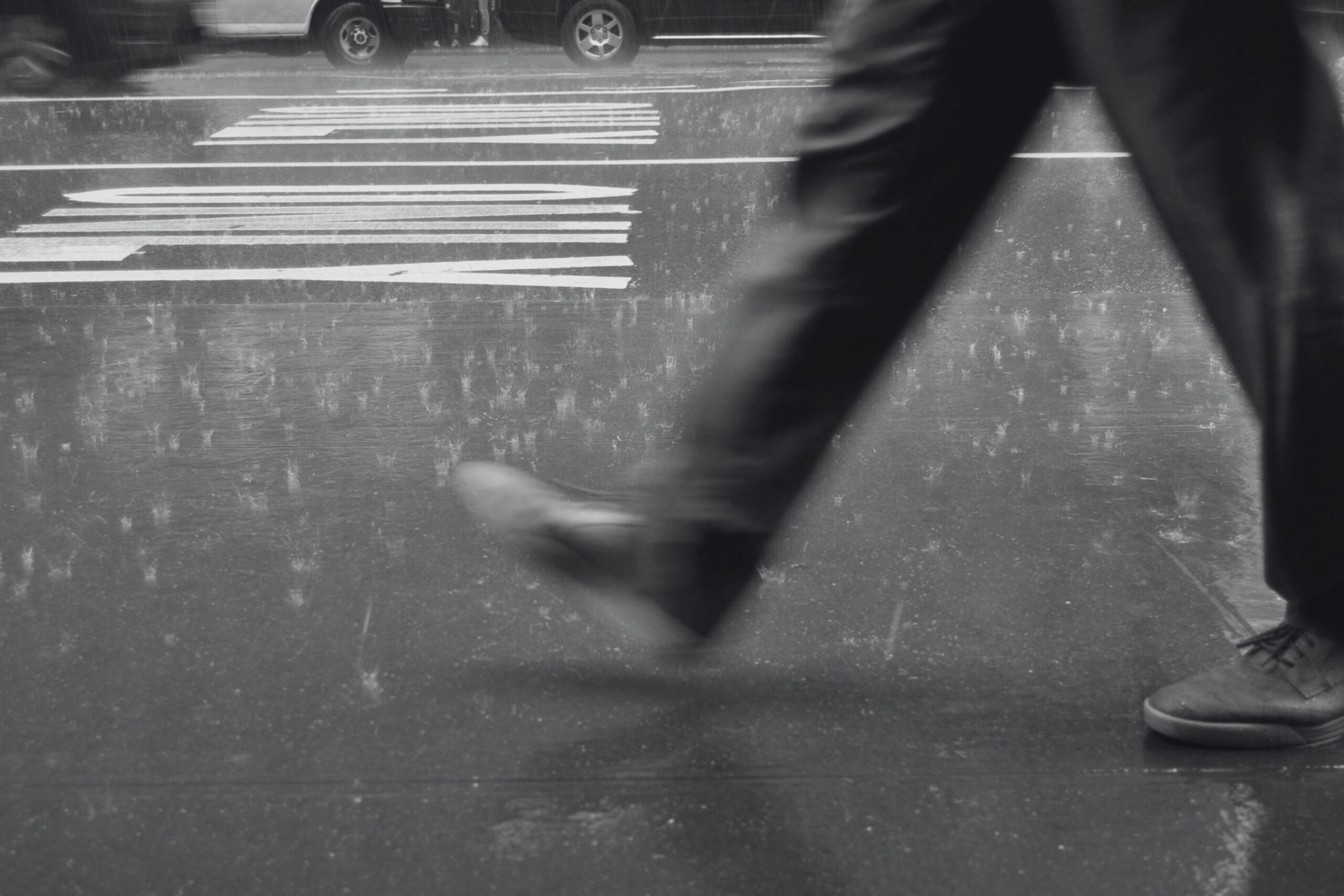 photo - black and white side angle shot of a man walking on the street up to his knees 